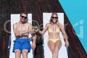 Couple sitting on sun lounger and toasting glass of mojito