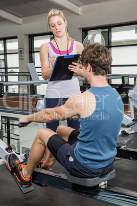 Trainer writing on a clipboard while man exercising on a rowing