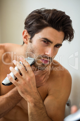 Young man shaving with trimmer