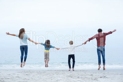 Family holding hands while jumping at sea shore