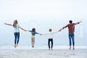 Family holding hands while jumping at sea shore
