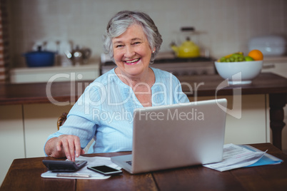 Smiling senior woman using calculator and laptop