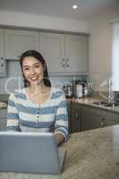 Portrait of young woman using a laptop in the kitchen