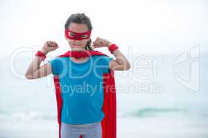Girl wearing superhero costume flexing muscles at beach
