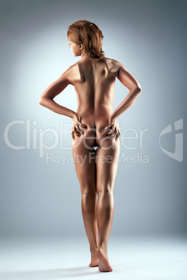 Nude slim woman with bronzed skin posing in studio