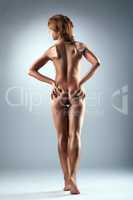 Nude slim woman with bronzed skin posing in studio