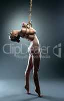 Studio shot of flexible nude girl hanging on rope