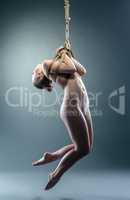 Skinny naked model hanging on rope in studio