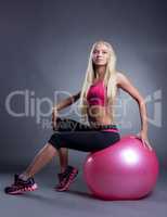 Beautiful young fitness trainer sitting on ball