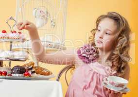 Smartly dressed little girl drinking tea with cake