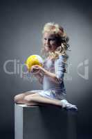 Cute blonde gymnast posing with ball on cube