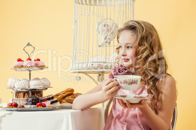 Pleased little girl drinking tea with cake in studio