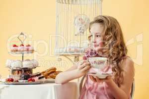 Pleased little girl drinking tea with cake in studio