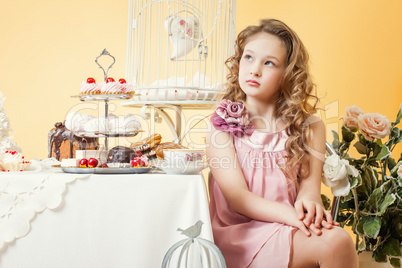 Thoughtful little lady posing at table with cakes