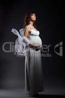 Dreamy pregnant woman posing in long white dress
