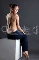 Pretty slim woman posing topless sitting on cube