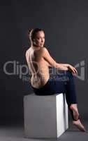 Slim topless girl sitting on cube, back to camera