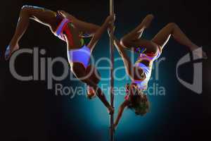 Sporty girls dancing on pole under UV light