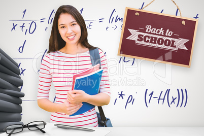 Composite image of college girl holding books with blurred stude