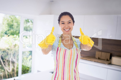 Composite image of happy woman giving thumbs up in rubber gloves