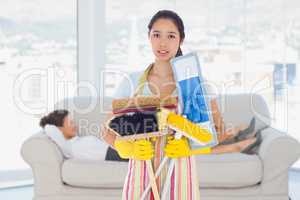 Composite image of frowning woman holding brushes and mops