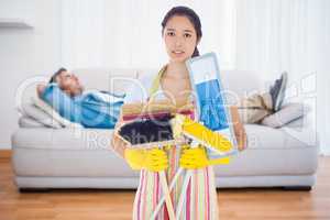 Composite image of frowning woman holding brushes and mops
