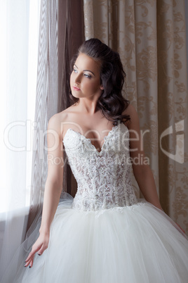 Pretty young bride posing by window in hotel room