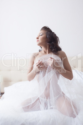 Sensual bride posing topless on bed in hotel room