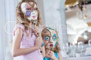 Cute sisters posing hiding faces behind masks