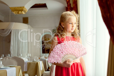 Elegant girl posing with fan standing at window