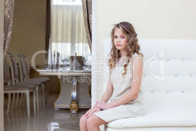 Elegant curly girl sitting on white leather sofa