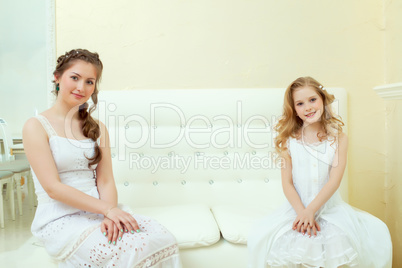 Lovely elegant sisters sitting on white couch