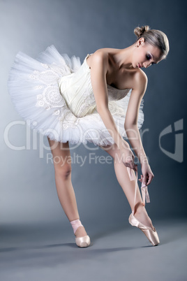 Beautiful young ballerina tying pointe in studio