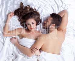 Pair of handsome young lovers lying on silk sheets