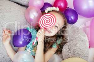 Playful curly girl hiding behind lollipop
