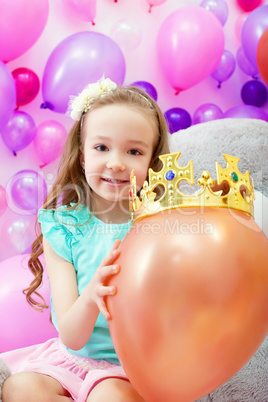 Cheerful girl playfully put crown on balloon