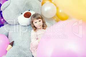 Serious little girl posing lying on big teddy bear