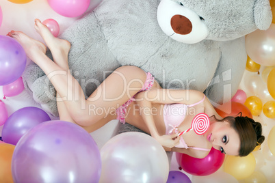 Playful model lying with lollipop on teddy bear