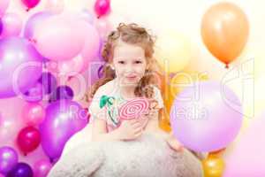 Adorable curly girl posing on balloons backdrop