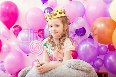 Lovely curly girl posing in crown with lollipop