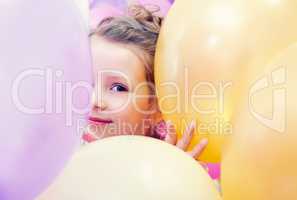 Cute little girl peeking out from behind balloons