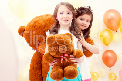 Pretty sisters posing with teddy bears in playroom