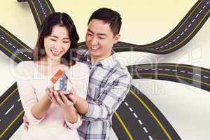 Composite image of happy couple holding a model house