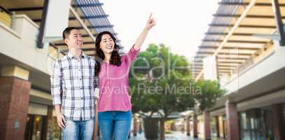 Composite image of happy couple pointing upwards