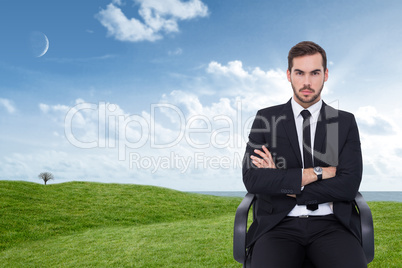 Composite image of serious businessman sitting with arms crossed