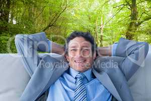Composite image of businessman smiling at camera sitting on couc