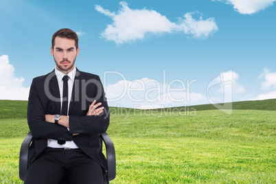 Composite image of serious businessman sitting with arms crossed