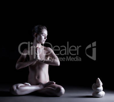 Nude girl with shimmering skin meditates in studio