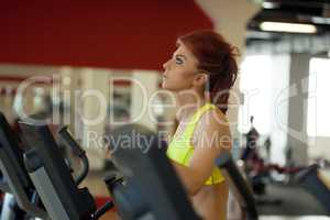 Pretty red-haired girl exercising on treadmill