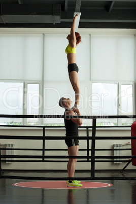 Strong acrobat holding his slender partner in gym